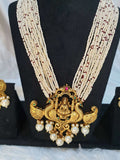 A display of traditional Indian jewelry, featuring a multi-string pearl haram with a gold-colored Lakshmi pendant, along with matching earrings with gold accents and pearls.