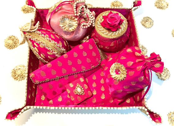 A collection of bridal trousseau gift set including metal boxes, bangles, and other wedding accessories, predominantly in pink and adorned with decorative elements.