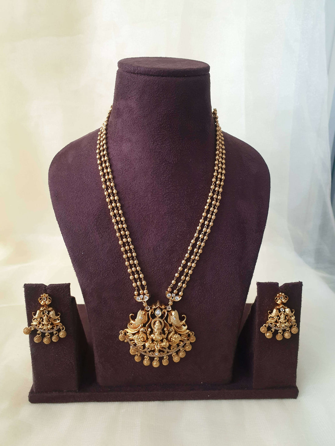 A gold-colored beaded Lakshmi Premium Pearl Mala Pendent Set with floral pendant drops and a pair of matching earrings displayed on a mannequin bust.
