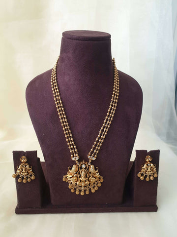 A gold-colored beaded Lakshmi Premium Pearl Mala Pendent Set with floral pendant drops and a pair of matching earrings displayed on a mannequin bust.