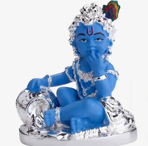 A blue-colored idol of Baby Krishna, known as Makhan Chor, sitting with a silver pot of butter, adorned with silver ornaments and a peacock feather in his hair.