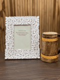 A white, floral-patterned, picture frame displayed next to a rustic wooden photo stand.