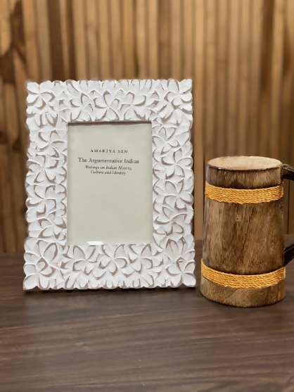 A white, floral-patterned, picture frame displayed next to a rustic wooden photo stand.
