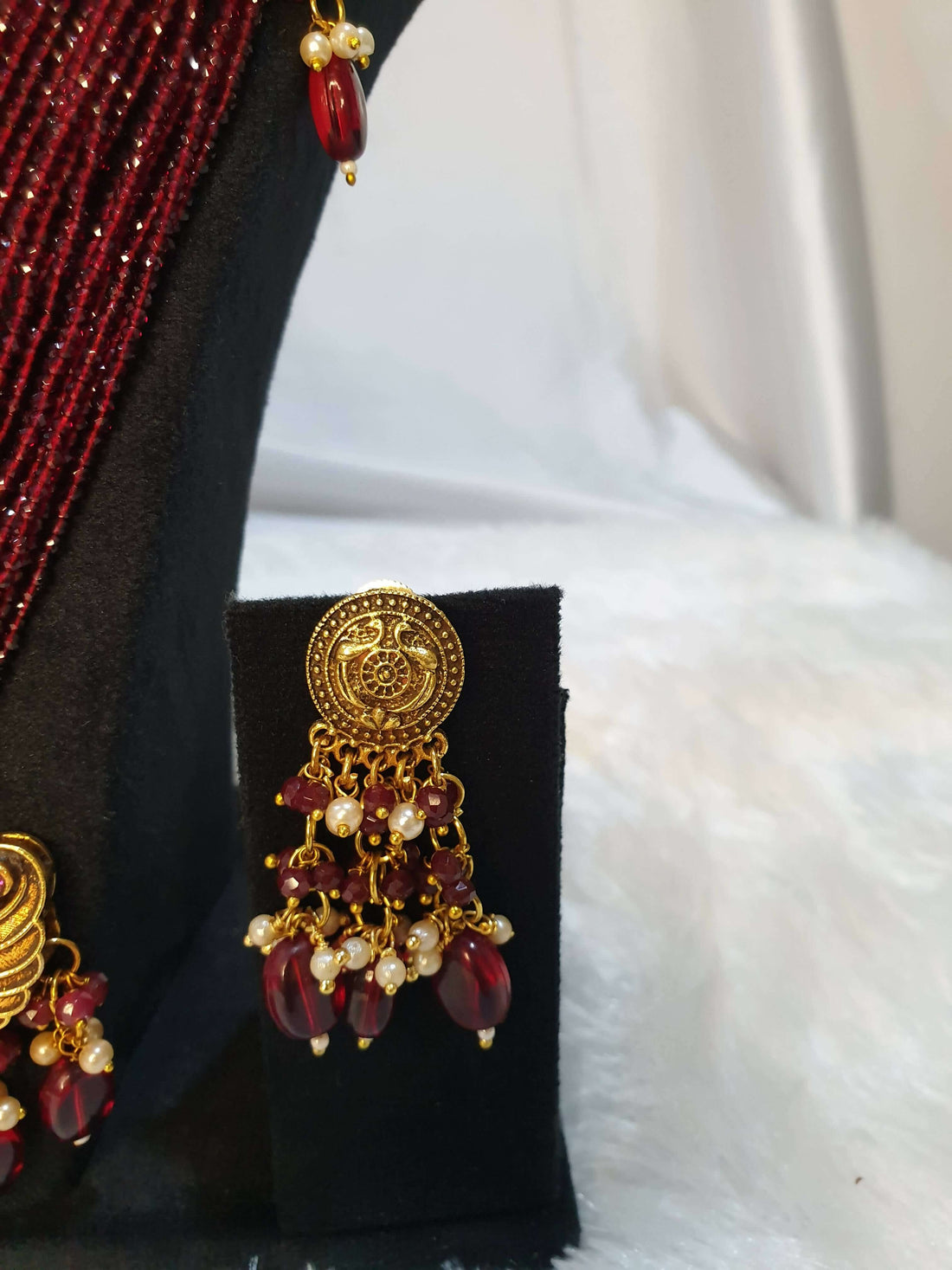 A multi-layered maroon necklace with gold detailing and a gold pendant, displayed on a mannequin with matching earrings.