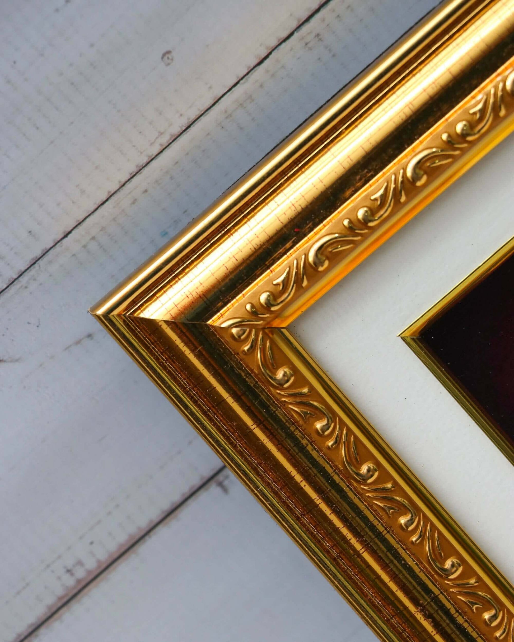 A close-up shot of an ornate golden picture frame with a white matte, resting on a light-colored wooden surface.