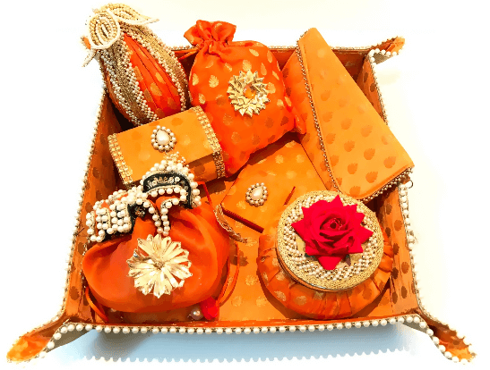 A collection of bridal trousseau gift set including metal boxes, bangles, and other wedding accessories, predominantly in orange and adorned with decorative elements.
