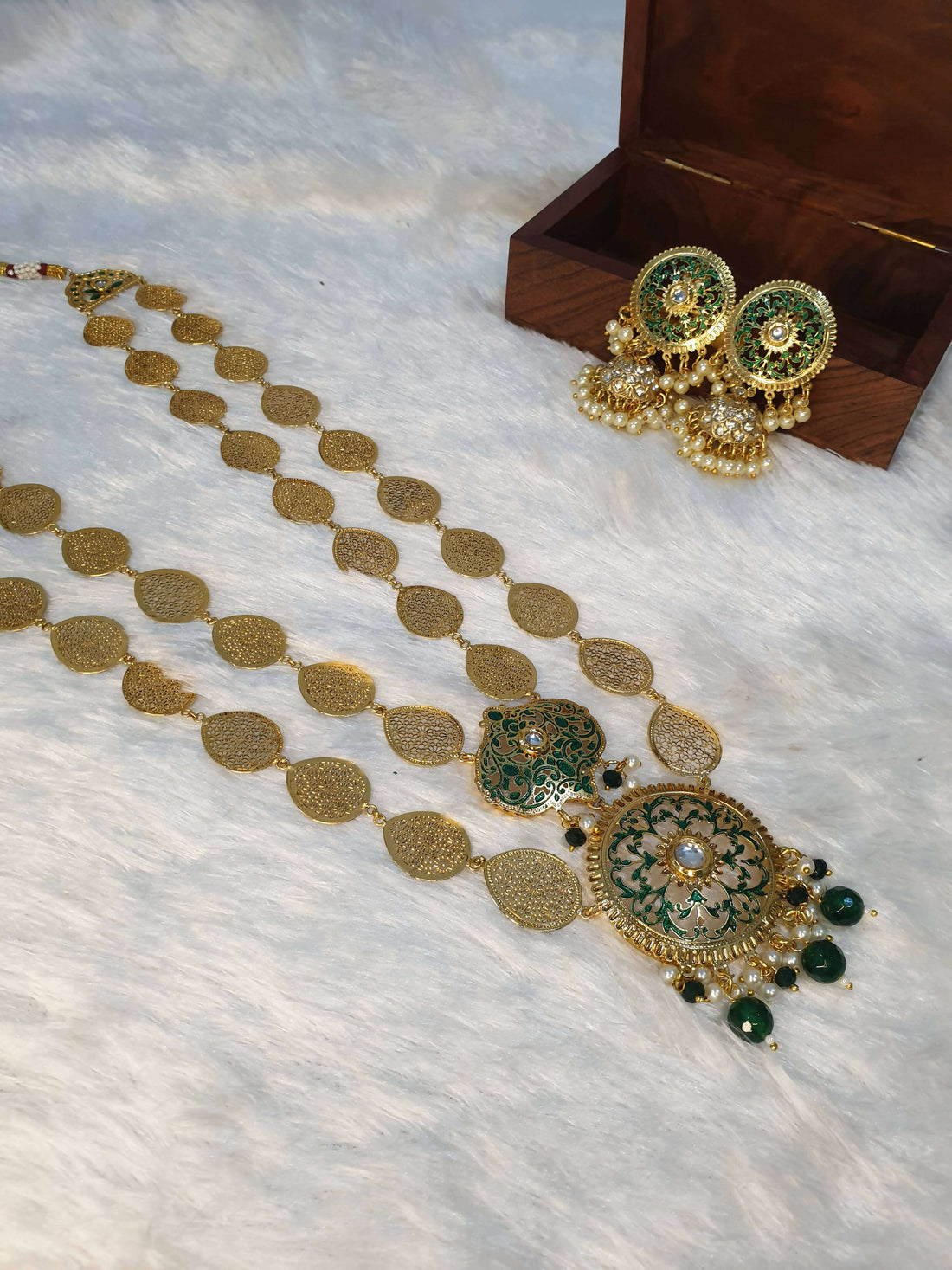 A gold-colored double layered filigree petals necklace accompanied by matching earrings, displayed on a white surface with a wooden box in the background.
