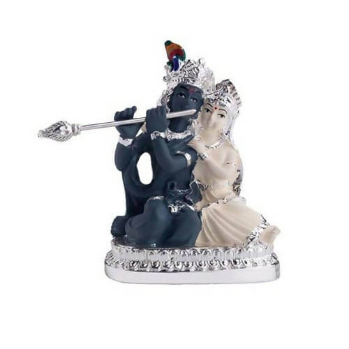A detailed idol depicting Lord Krishna playing the flute while seated next to Radha, who is adorned with elaborate jewelry and garments, likely a decorative showpiece.