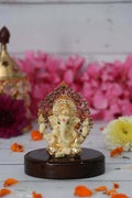 A cream and gold Ganesha idol with a detailed Kalpavriksha Tree halo, seated on a glossy dark wooden base.
