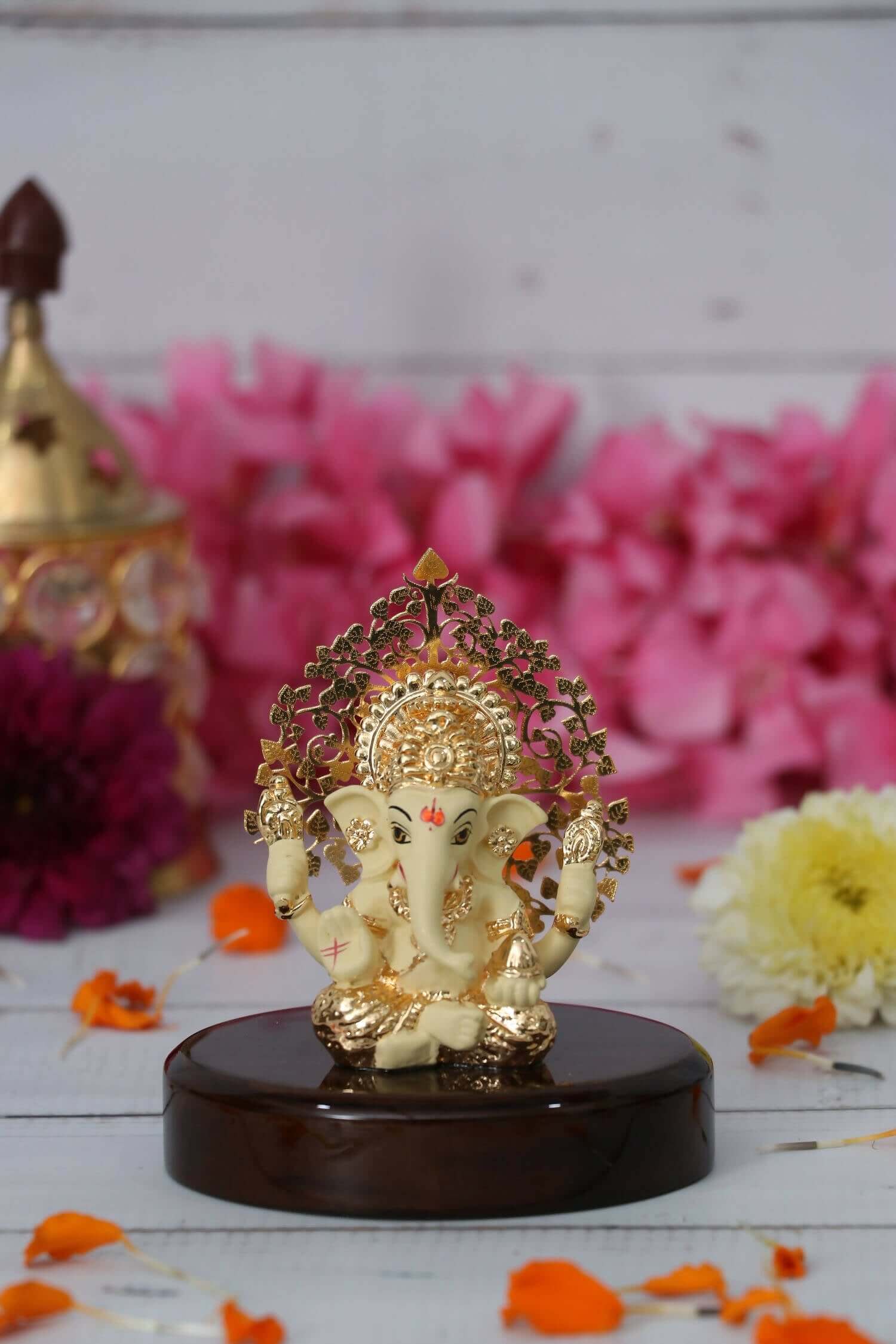 A cream and gold Ganesha idol with a detailed Kalpavriksha Tree halo, seated on a glossy dark wooden base.