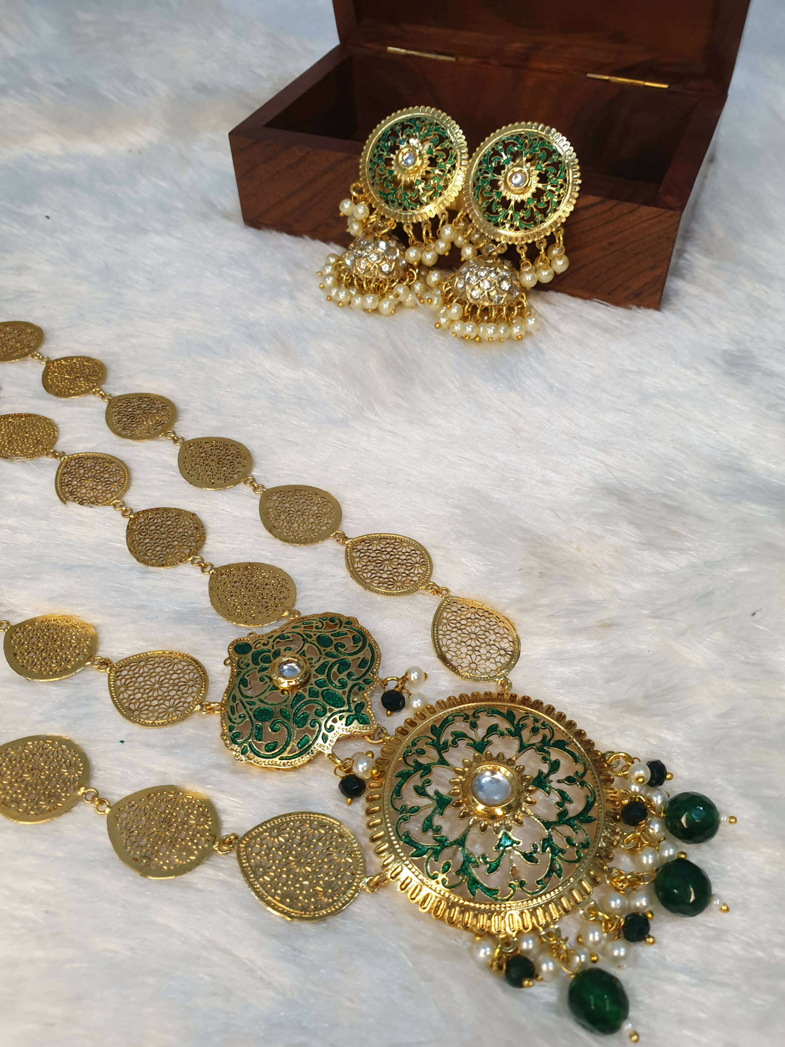 A gold-colored double layered filigree petals necklace accompanied by matching earrings, displayed on a white surface with a wooden box in the background.