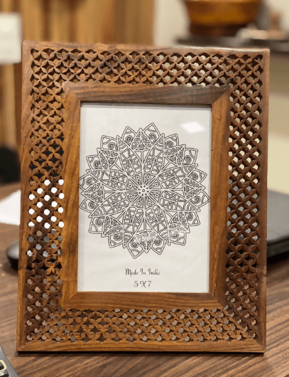 Handcrafted Sheesham wood photo frame with a geometric design, displaying a photo within it, placed on a table.