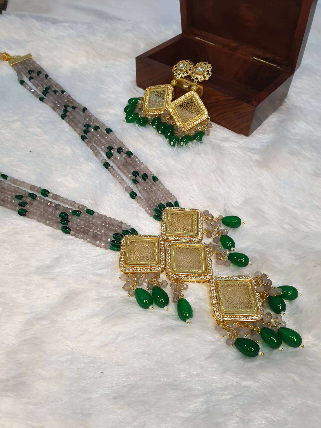 A long beaded necklace with pearl adornments and a unique pendant design, displayed alongside a wooden box.