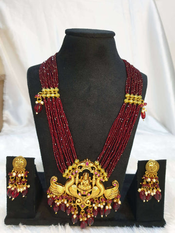 A multi-layered maroon necklace with gold detailing and a gold pendant, displayed on a mannequin with matching earrings.