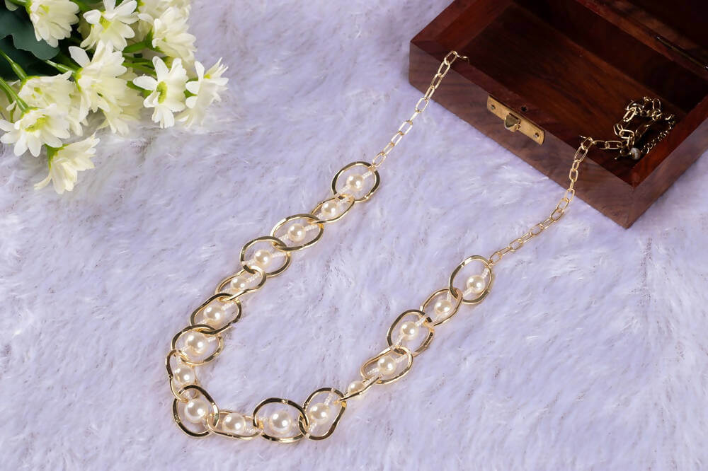 A handwrapped statement necklace with circular crystal beads in brown and beige colors, displayed on a plush white surface next to a wooden box and floral arrangement.