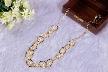 A handwrapped statement necklace with circular crystal beads in brown and beige colors, displayed on a plush white surface next to a wooden box and floral arrangement.