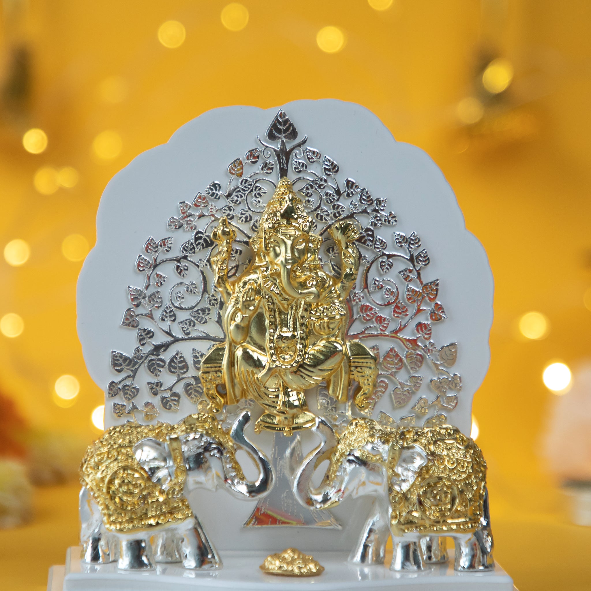 A golden and silver showpiece depicting a Kalpavriksha Tree Ganesha Idol with Lord Ganesha seated in front of a silver and gold tree, flanked by two elephants on a white base.