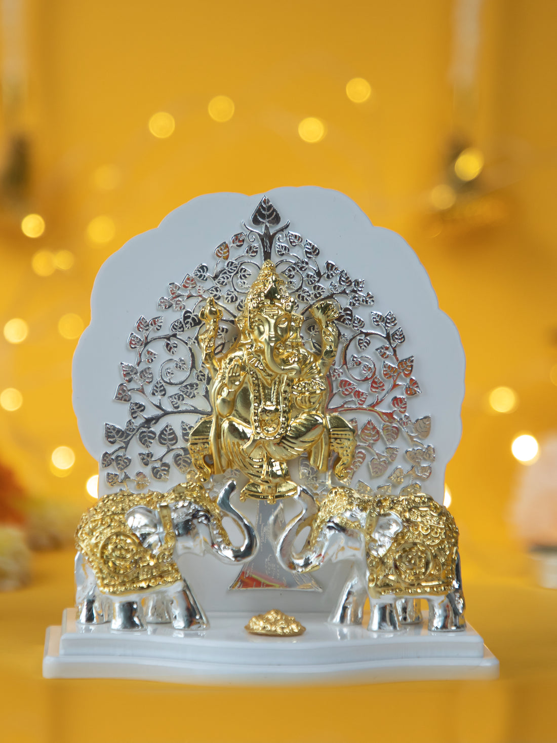 A golden and silver showpiece depicting a Kalpavriksha Tree Ganesha Idol with Lord Ganesha seated in front of a silver and gold tree, flanked by two elephants on a white base.