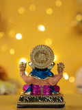 Dagdusheth Ganpati Idol, a miniature statue of Lord Ganesha, is shown from the back. The idol features a golden-colored headpiece and hands, a blue and pink dhoti, and sits on a golden platform, with a bokeh background of yellow lights.