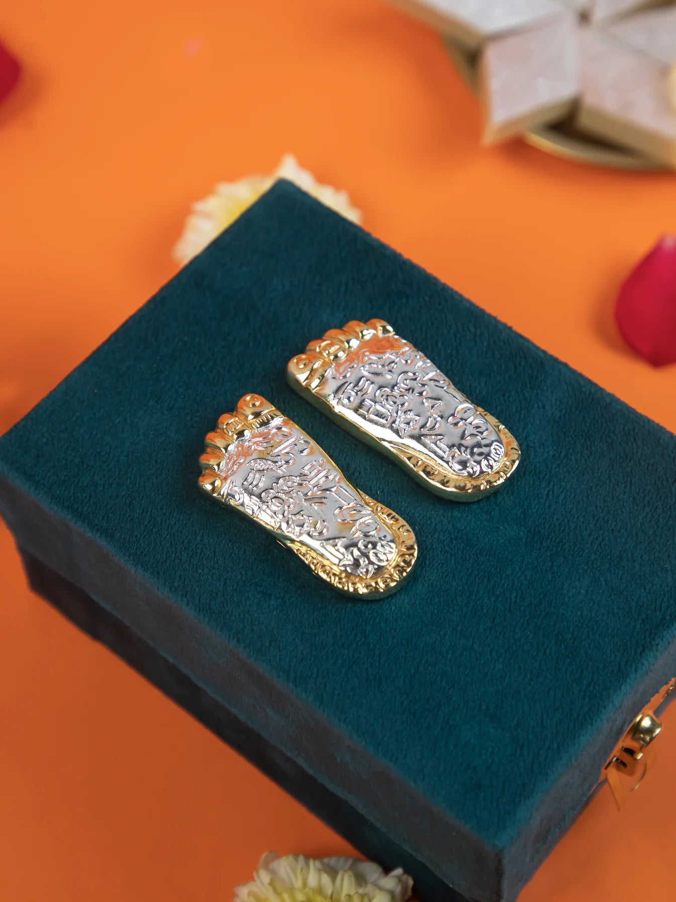 A pair of gold and silver-plated Laxmi Charan Paduka, which are symbolic footprints of the Hindu goddess Lakshmi, placed on a dark green velvet box". The Laxmi Charan Paduka are a sacred symbol representing the goddess's presence and are believed to bring prosperity, wealth, and good fortune.