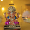 decorative Dagdusheth Ganpati Idol, a seated Ganesha statue that is 3 inches wide and 3.5 inches tall, with a pinkish-orange body, blue clothes, and gold accents. The idol sits on a gold base with a decorative halo behind the head. It is a popular idol, often used for home decor, worship, or as a gift.
