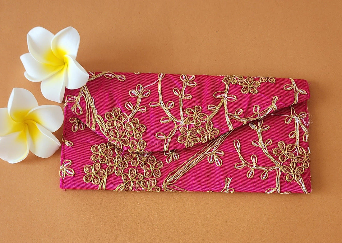 A red envelope with gold floral embroidery, placed on an orange surface with two white flowers at the top left corner.