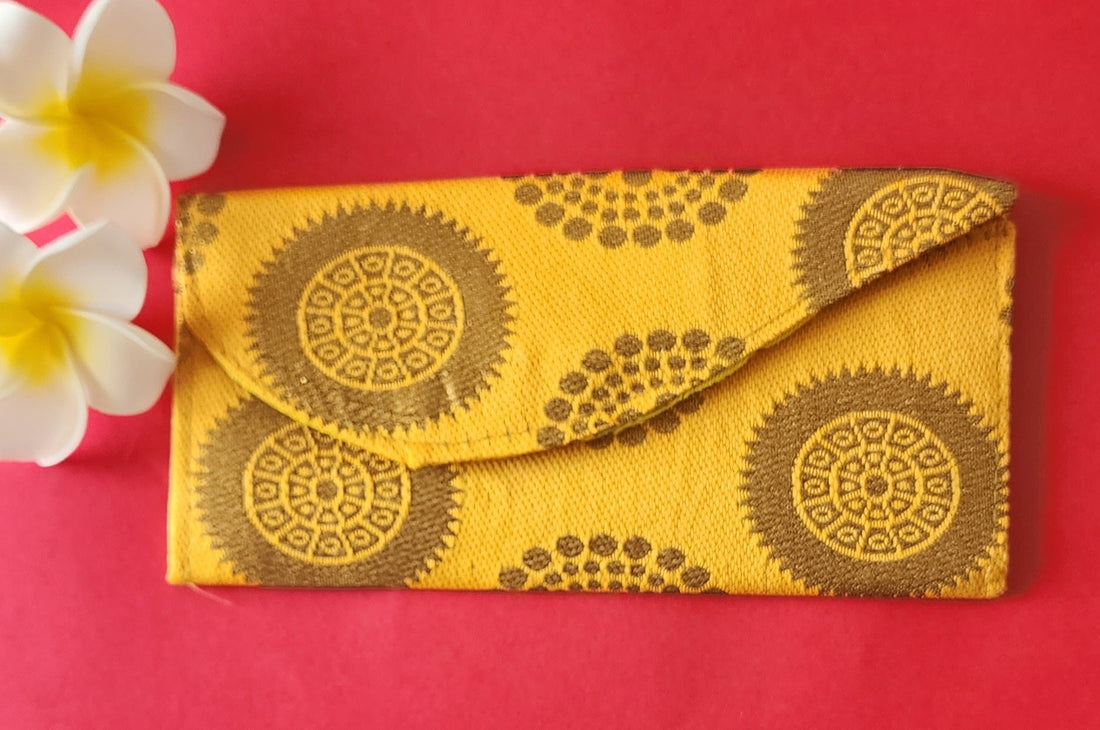 A green envelope with traditional block print patterns displayed on a yellow background, accompanied by a white flower with a yellow pistil.