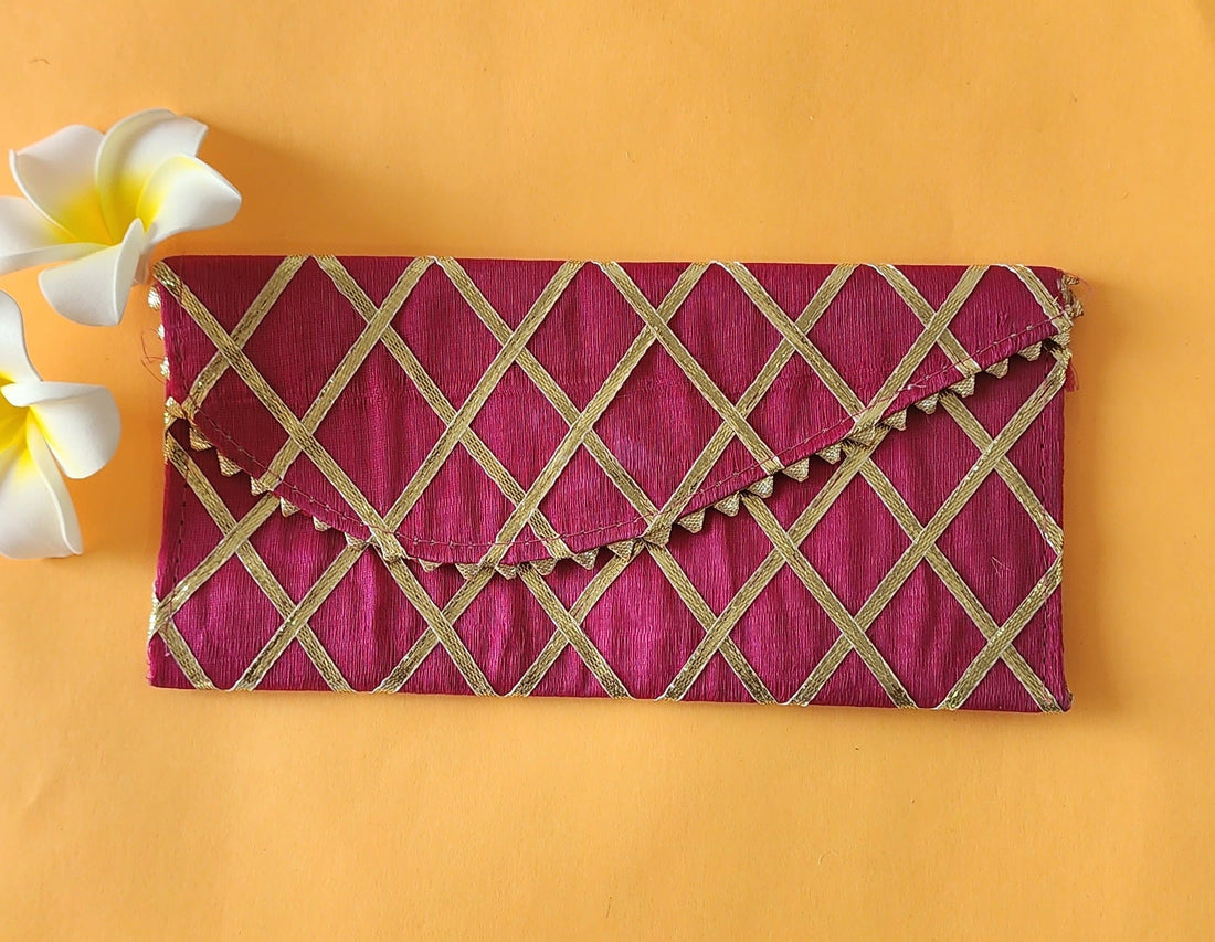 An orange envelope with a crisscross geometric pattern, displayed on a flat surface with a few flowers beside it.