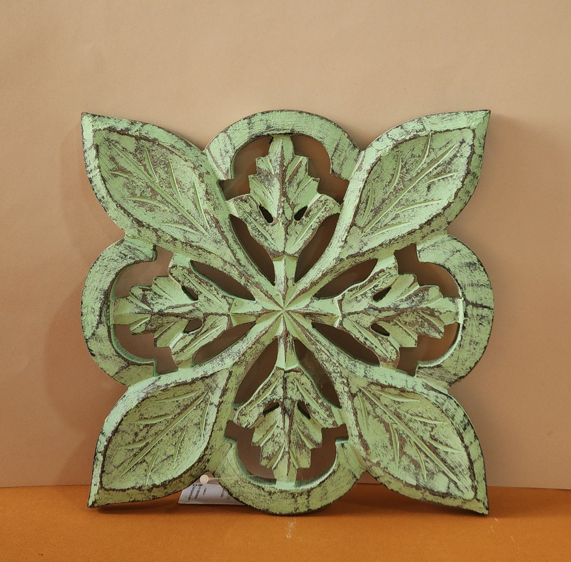 A wooden carved trivet with a green finish, featuring intricate leaf patterns.