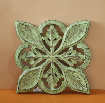 A wooden carved trivet with a green finish, featuring intricate leaf patterns.