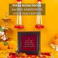 A framed image of the Mahamrityunjaya Mantra on a red background is surrounded by traditional Hindu puja items, including a lit oil lamp (diya), flowers, and a bell. The image has a text overlay that reads 