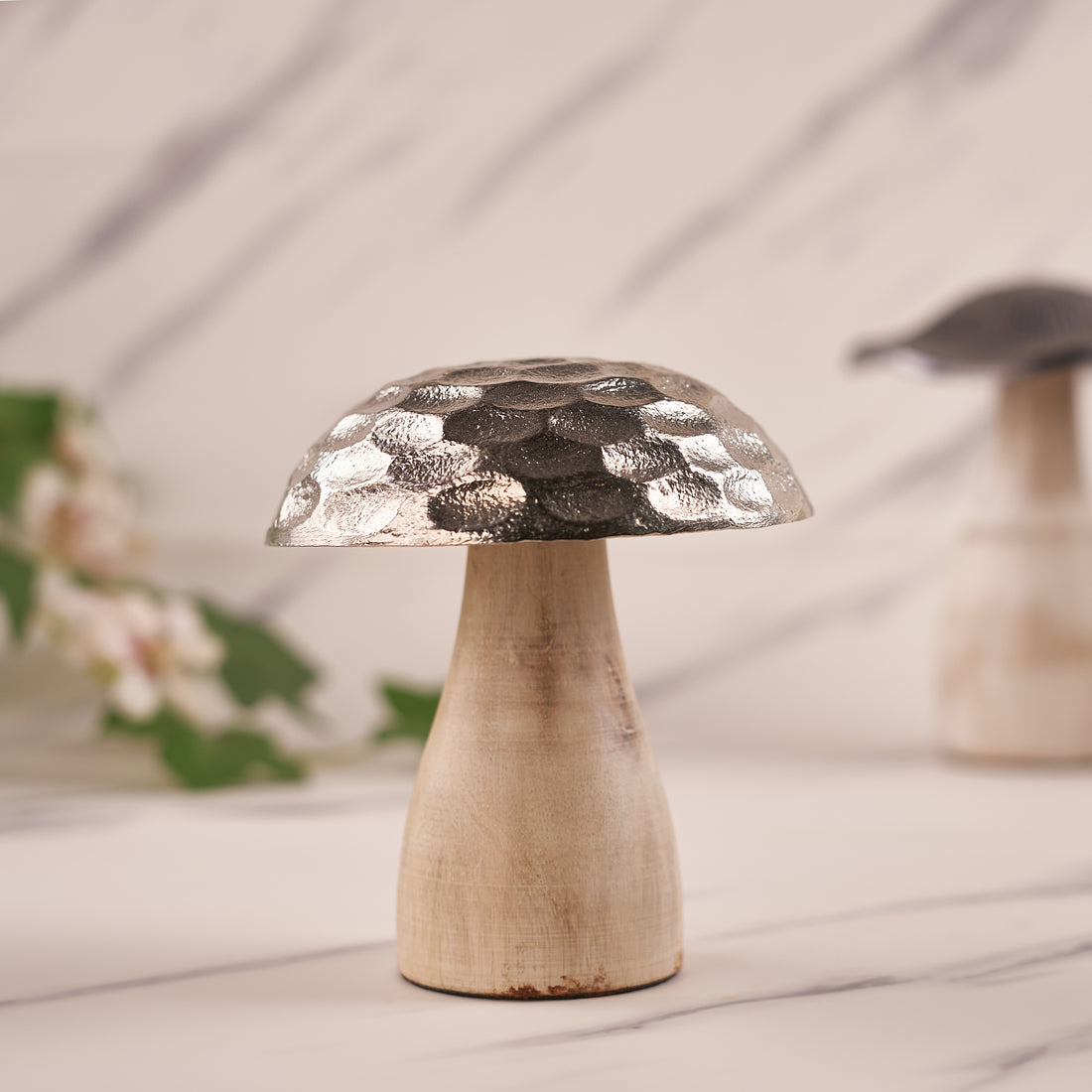 A decorative mushroom with a silver hammered pattern on the top cap, placed on a wooden stem, against a neutral background.