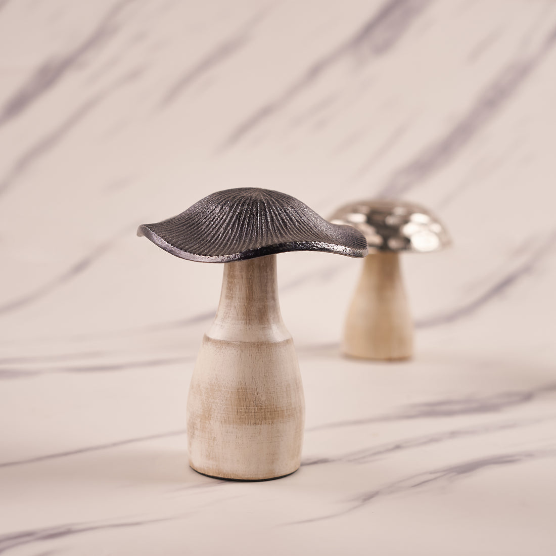 A silver mushroom-shaped decorative metal piece with an engraved pattern, displayed on a marble surface.