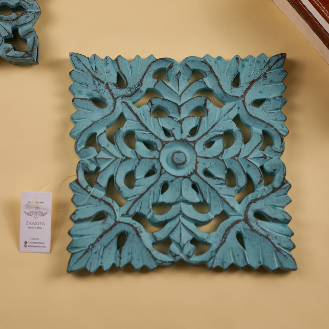 A turquoise wooden carved trivet with intricate floral patterns, displayed on a yellow background.