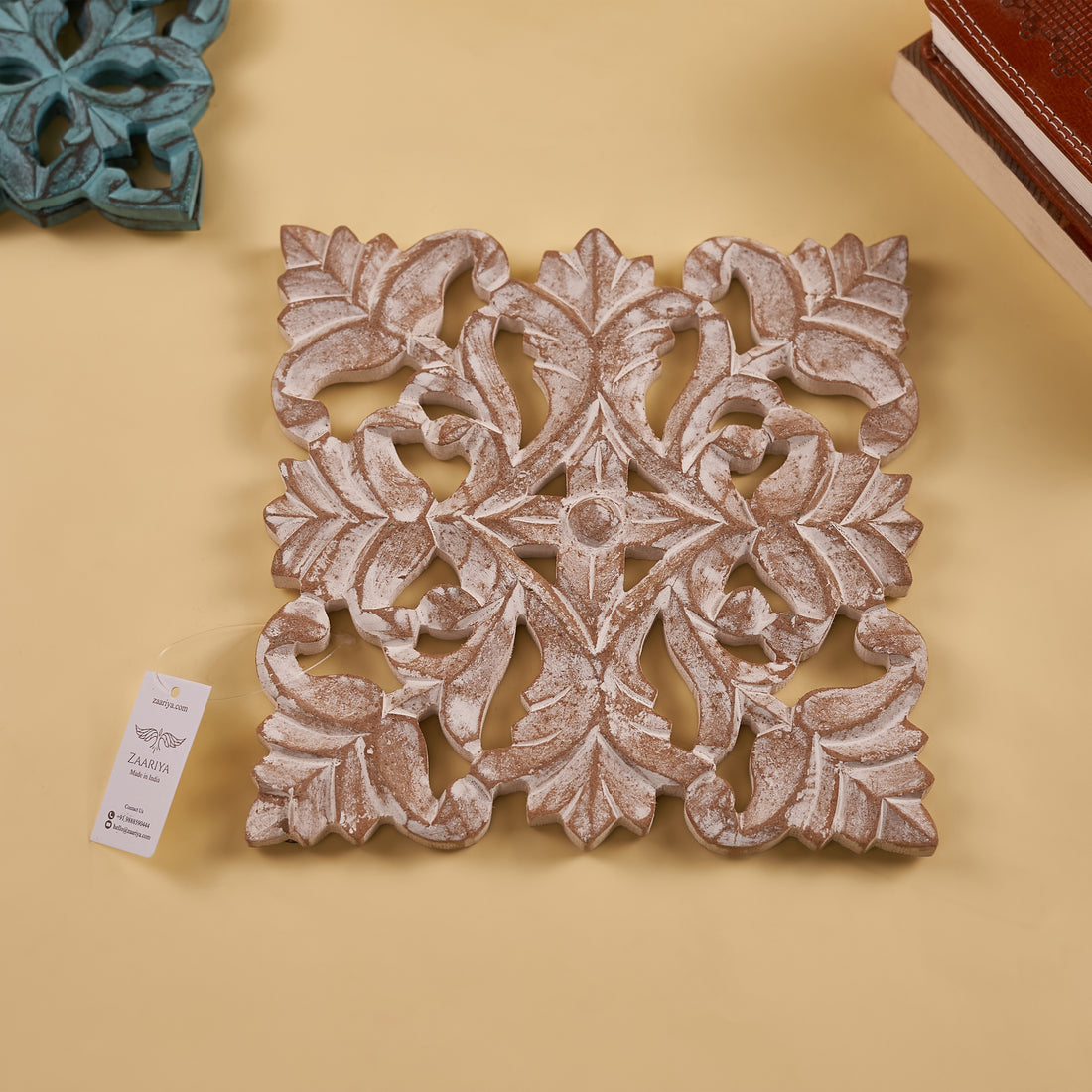 A wooden carved trivet with an antique white finish, featuring intricate floral patterns, displayed on a yellow background.