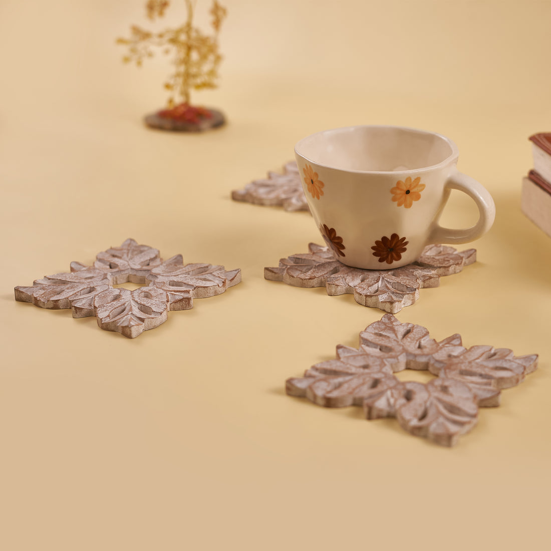 A set of four white wooden coasters with carved leaf patterns, displayed on a yellow background.
