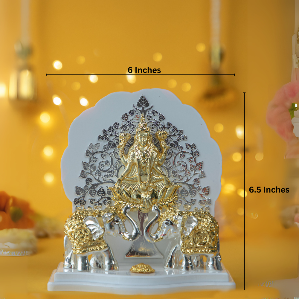 Gajalakshmi idol made of silver and gold-plated material, featuring the goddess Lakshmi seated on a lotus, flanked by two elephants with raised trunks, against a backdrop of a detailed tree design.