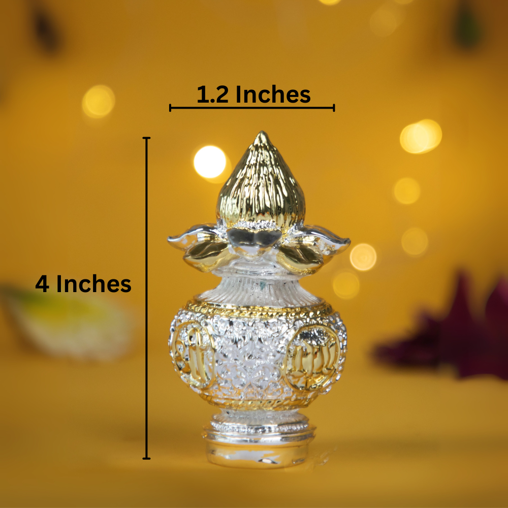 A small, decorative silver and gold-plated kalash with a coconut on top, nestled in a plush, dark teal velvet box with a gold clasp. The item is displayed on a yellow surface with scattered flower petals and is used for puja, gifting, and home decor.