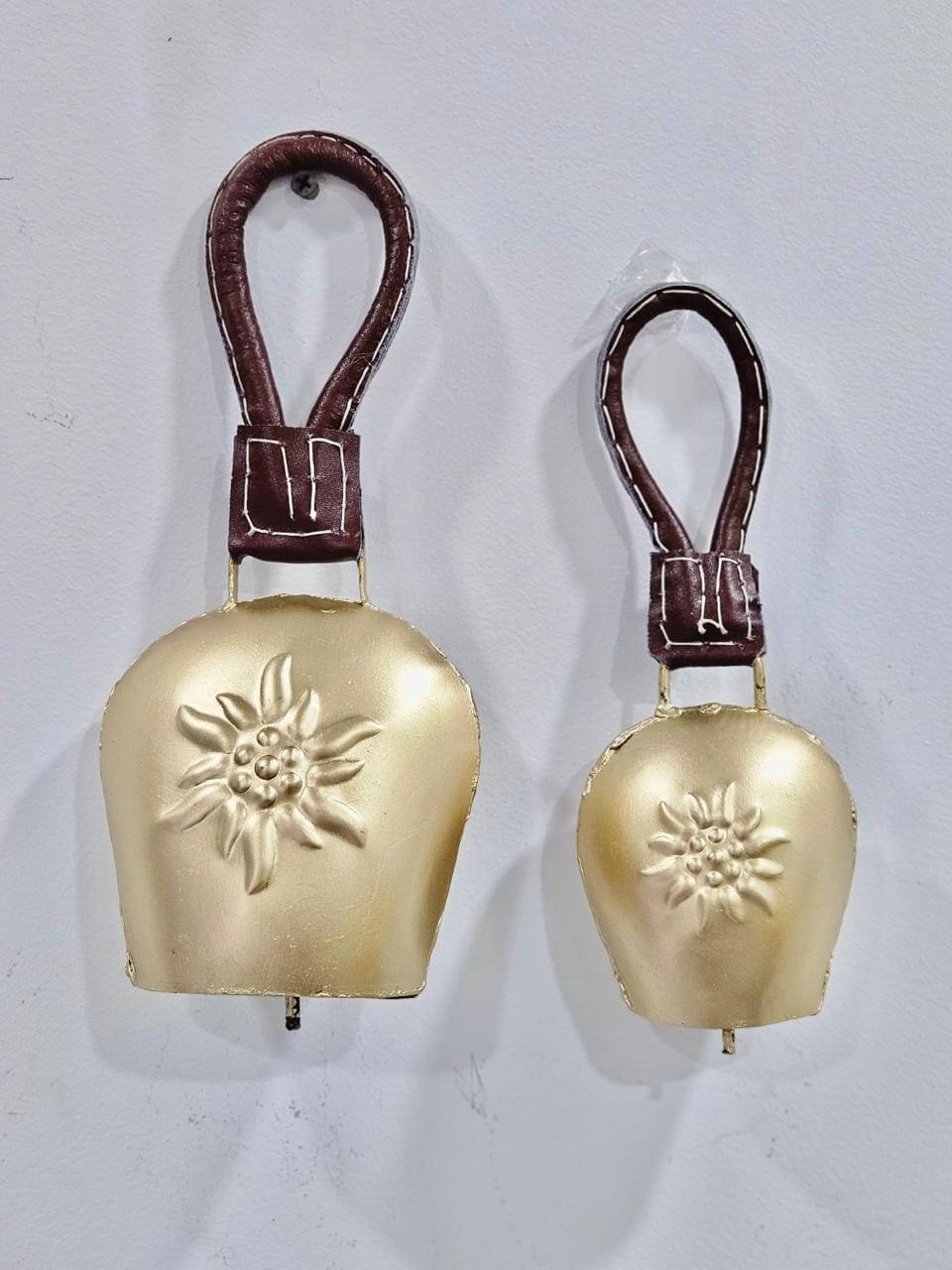 Two bronze-colored iron chimes with a floral pattern, one larger and one smaller, each with a leather strap attached.